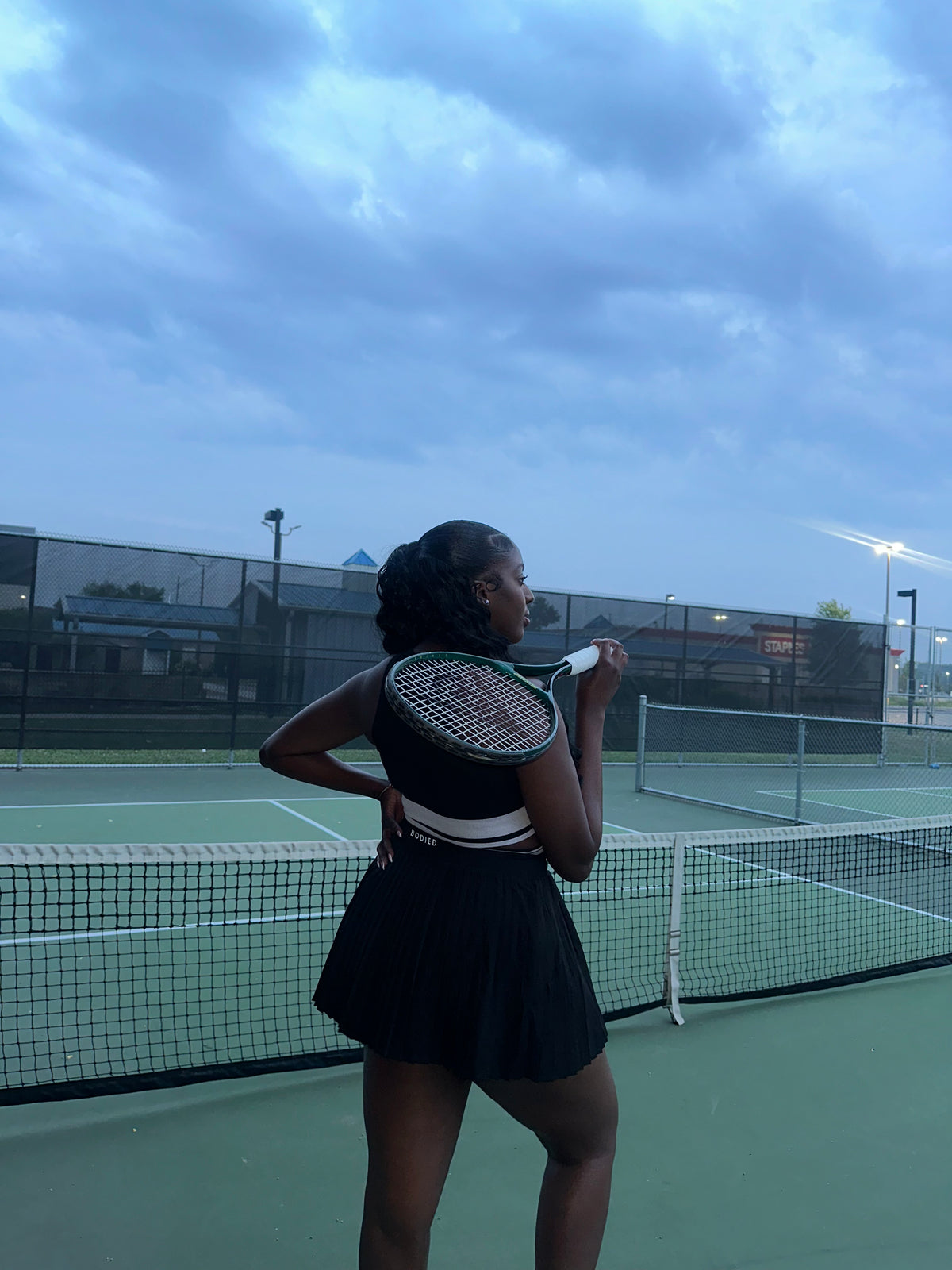 Person holding a tennis racket on a tennis court with a blue sky in the background