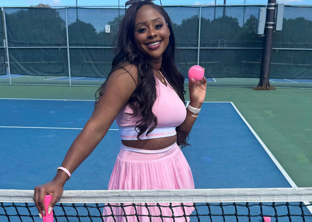 Woman in pink tennis outfit holding a pink tennis racket and ball on a tennis court.