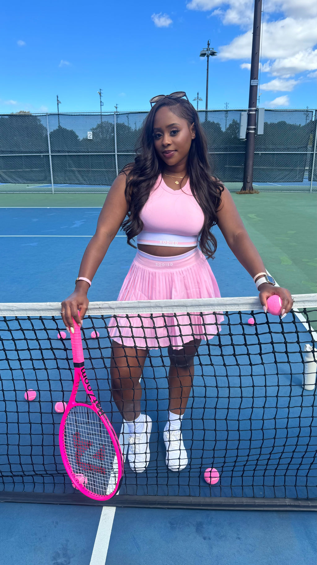 Woman in pink tennis outfit holding a pink tennis racket and balls on a tennis court.